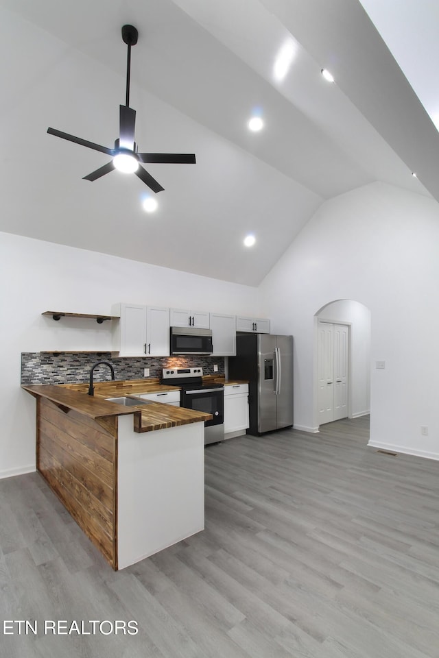 kitchen with stainless steel appliances, backsplash, white cabinetry, light wood-type flooring, and a peninsula