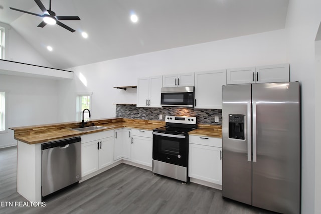 kitchen featuring open shelves, stainless steel appliances, butcher block counters, a sink, and a peninsula