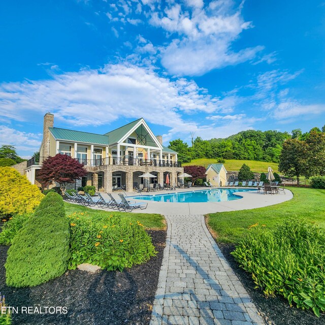 rear view of property with a patio, a balcony, a community pool, and a lawn