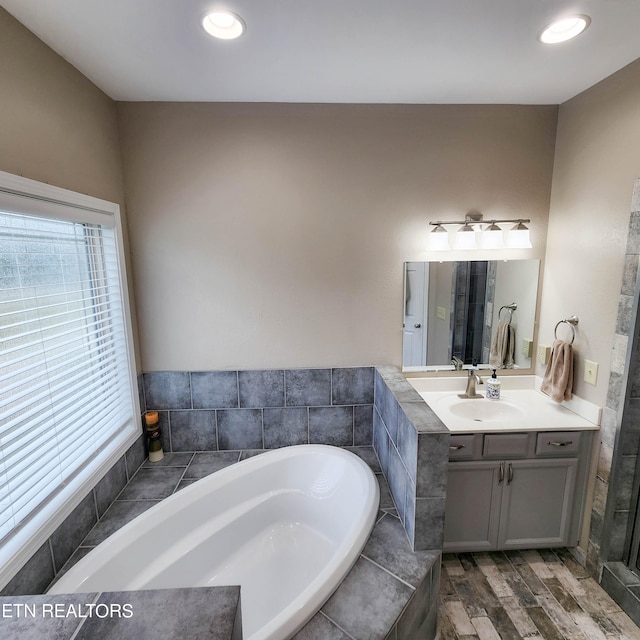 bathroom with vanity, a relaxing tiled tub, and wood-type flooring