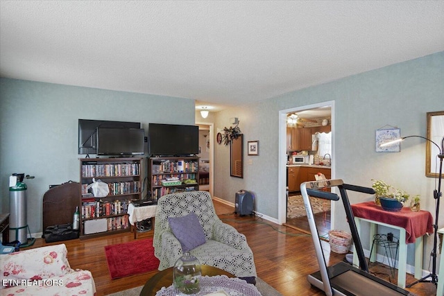 living area with a textured ceiling, dark wood-type flooring, and baseboards