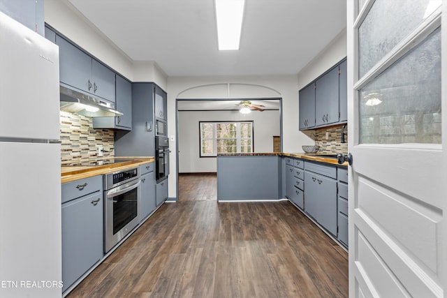 kitchen featuring butcher block countertops, dark wood-type flooring, under cabinet range hood, black appliances, and backsplash