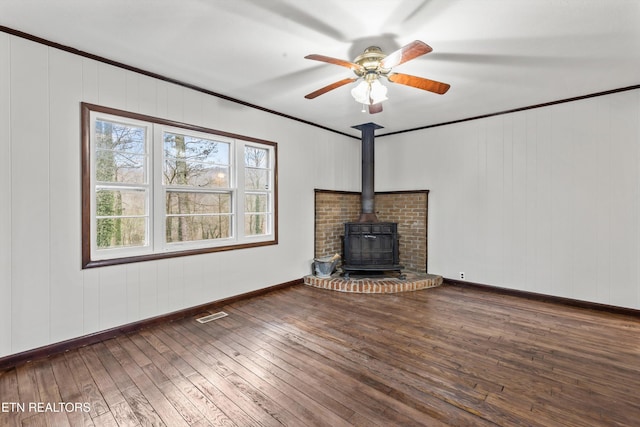 unfurnished living room with visible vents, baseboards, hardwood / wood-style flooring, ornamental molding, and a wood stove