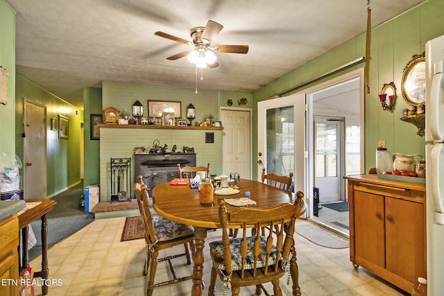 dining area with ceiling fan, light floors, and a brick fireplace