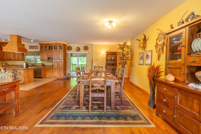 dining area featuring light wood finished floors, a textured ceiling, and baseboards