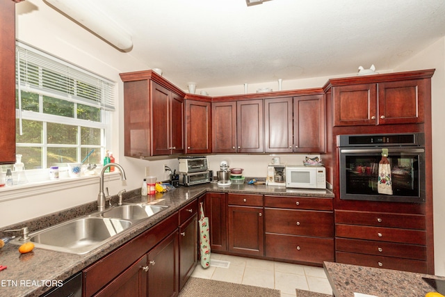 kitchen with sink, oven, dishwasher, light tile patterned floors, and dark stone counters