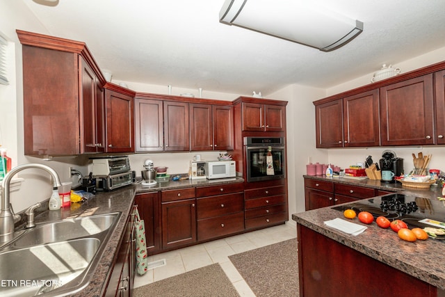 kitchen featuring dark stone countertops, light tile patterned floors, black electric cooktop, sink, and oven