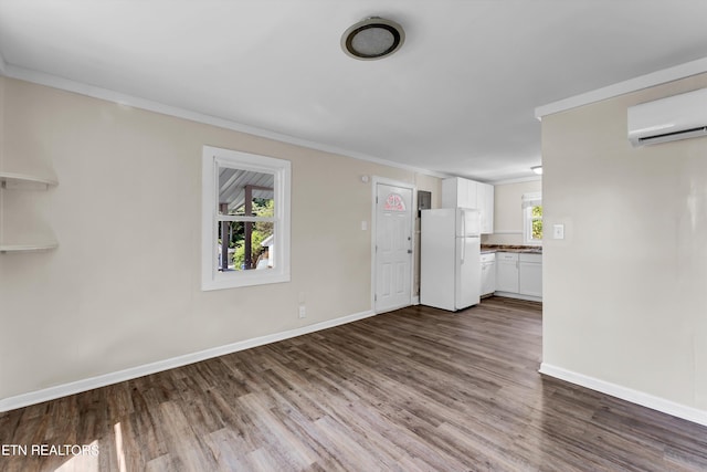 unfurnished living room featuring ornamental molding, dark wood-type flooring, a wall mounted air conditioner, and baseboards