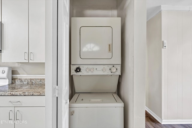 washroom featuring stacked washer / drying machine, laundry area, and wood finished floors