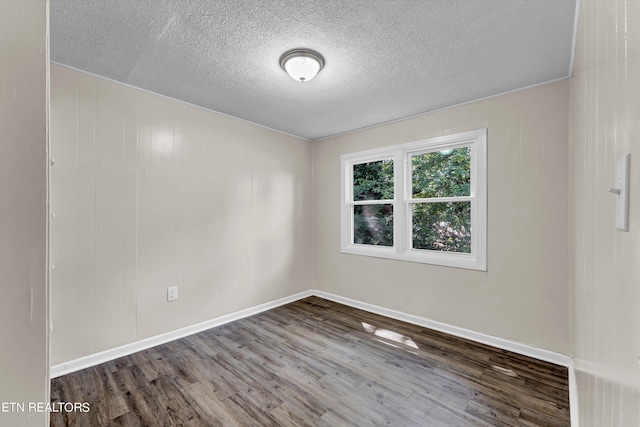 spare room featuring a textured ceiling, wood finished floors, and baseboards