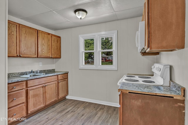 kitchen featuring light wood-style floors, brown cabinetry, a sink, white appliances, and a drop ceiling