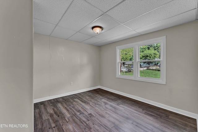 unfurnished room featuring dark wood-style flooring, a drop ceiling, and baseboards