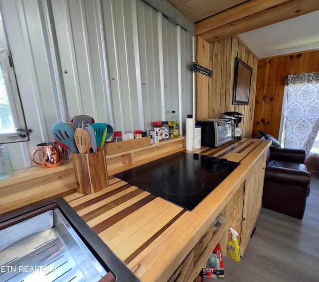 kitchen with hardwood / wood-style flooring, black electric stovetop, and wood walls