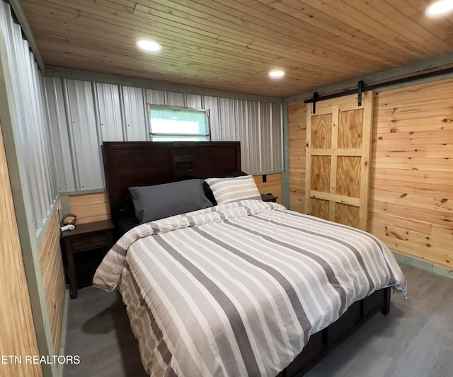 bedroom with hardwood / wood-style floors, a barn door, wooden ceiling, and wood walls