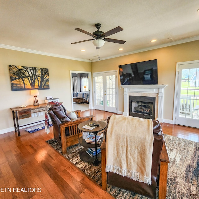 living room with ceiling fan, a tiled fireplace, a healthy amount of sunlight, and wood-type flooring