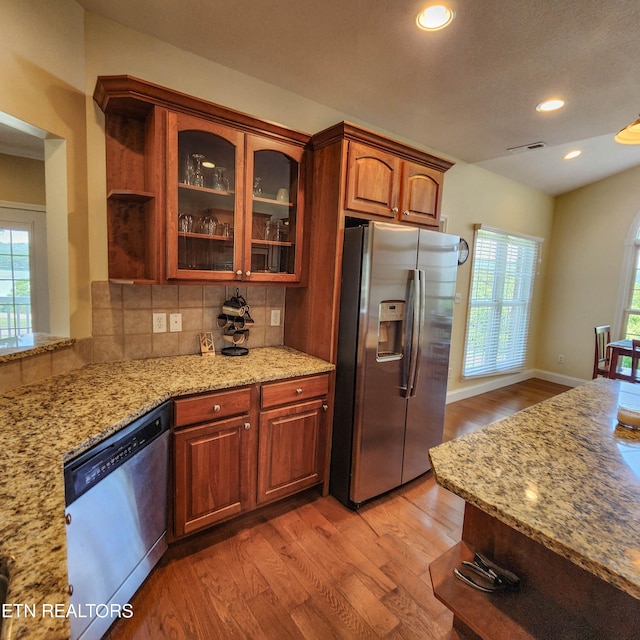 kitchen with appliances with stainless steel finishes, plenty of natural light, light hardwood / wood-style flooring, and decorative backsplash