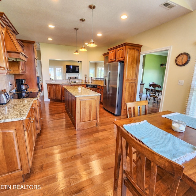 kitchen with stainless steel fridge, tasteful backsplash, light hardwood / wood-style floors, light stone counters, and a center island