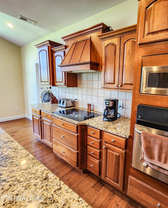 kitchen with decorative backsplash, custom range hood, wood-type flooring, light stone countertops, and stainless steel appliances