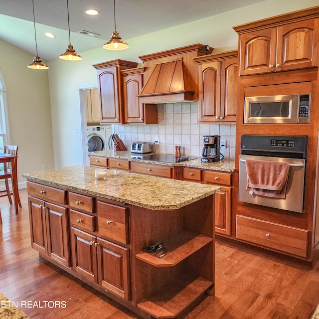 kitchen with hardwood / wood-style floors, backsplash, custom exhaust hood, washer and dryer, and stainless steel appliances