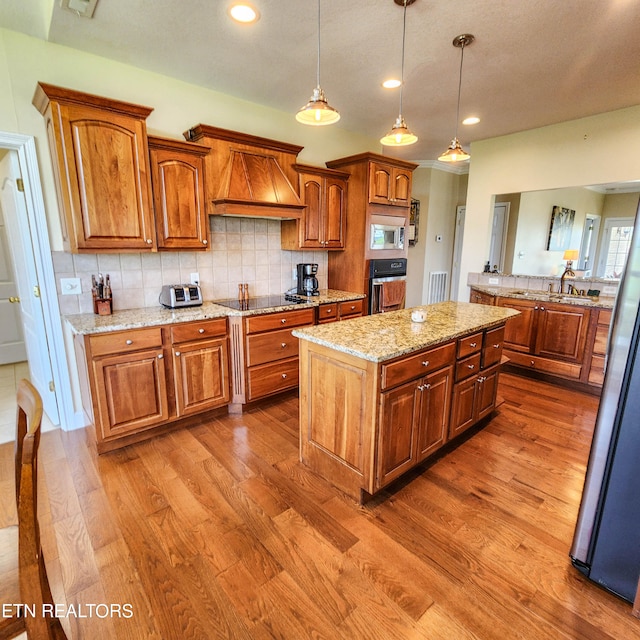 kitchen with hardwood / wood-style flooring, custom exhaust hood, tasteful backsplash, a kitchen island, and black appliances