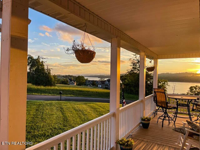 deck at dusk featuring a lawn and a water view