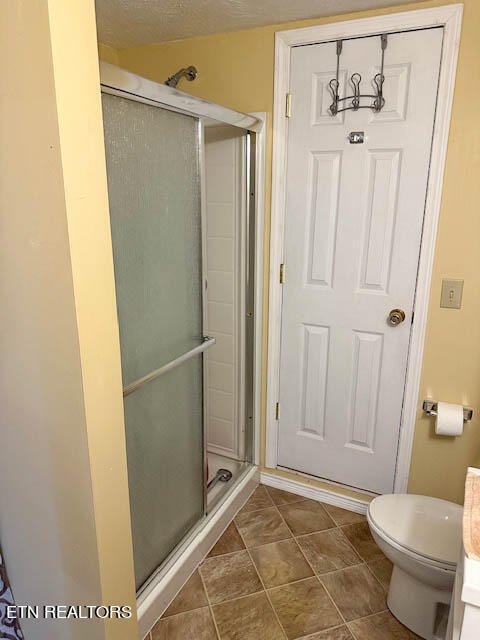 bathroom featuring toilet, an enclosed shower, tile patterned floors, and a textured ceiling