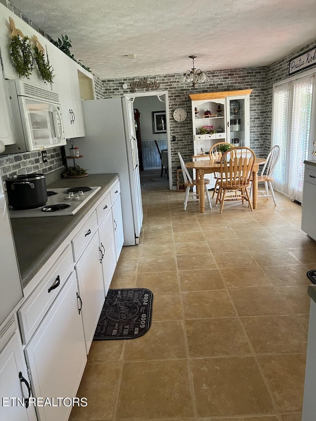 kitchen featuring light tile patterned floors, brick wall, a textured ceiling, and white cabinetry