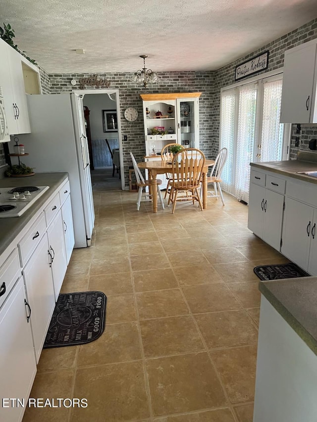 kitchen featuring a textured ceiling, brick wall, and white cabinets