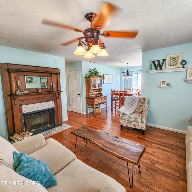 living room featuring ceiling fan with notable chandelier, hardwood / wood-style floors, a textured ceiling, and a fireplace