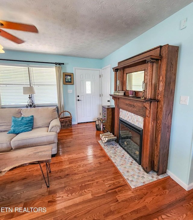 living room with a textured ceiling, a tiled fireplace, wood finished floors, and baseboards