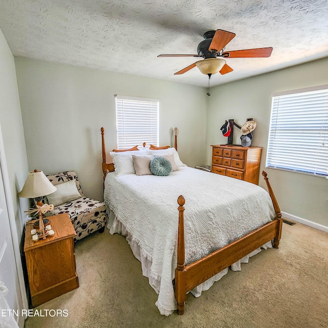 carpeted bedroom with a textured ceiling, multiple windows, visible vents, and a ceiling fan