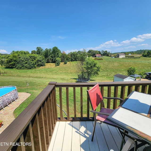 wooden deck with a rural view, a yard, and a trampoline