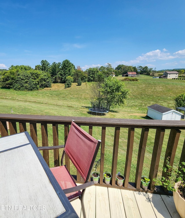 wooden terrace featuring a lawn, a storage shed, and a trampoline