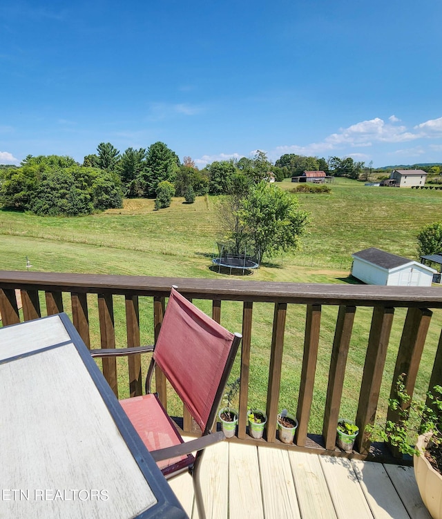 wooden deck featuring a rural view, a yard, and a trampoline