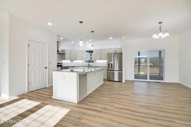 kitchen with appliances with stainless steel finishes, wall chimney exhaust hood, light hardwood / wood-style flooring, a center island, and hanging light fixtures