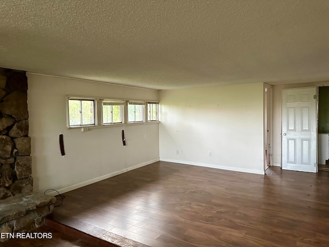 spare room featuring a textured ceiling, dark wood-type flooring, and a stone fireplace