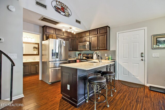 kitchen with appliances with stainless steel finishes, dark hardwood / wood-style floors, kitchen peninsula, dark brown cabinetry, and a breakfast bar