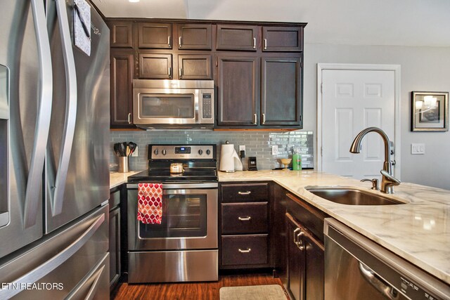 kitchen with light stone countertops, dark brown cabinets, appliances with stainless steel finishes, dark wood-type flooring, and sink