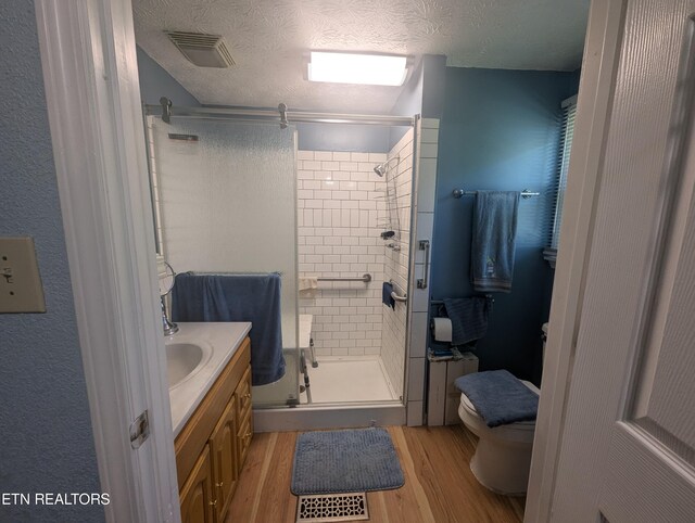 bathroom with a textured ceiling, walk in shower, hardwood / wood-style floors, vanity, and toilet