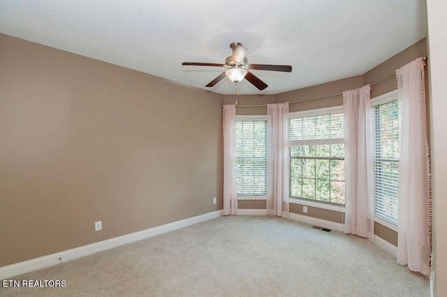 empty room with light carpet, a ceiling fan, visible vents, and baseboards