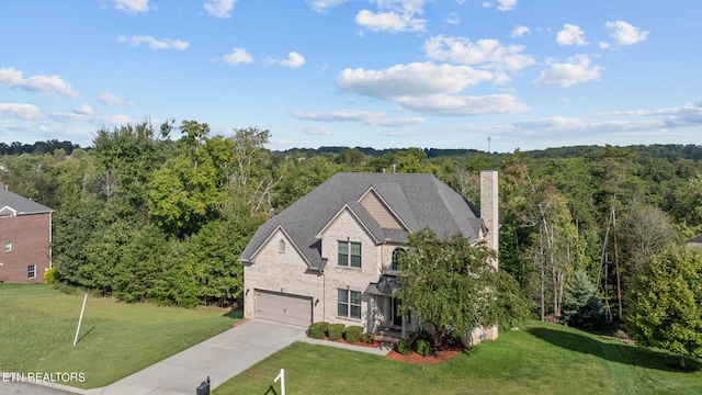 view of front facade with a front yard, concrete driveway, and a forest view