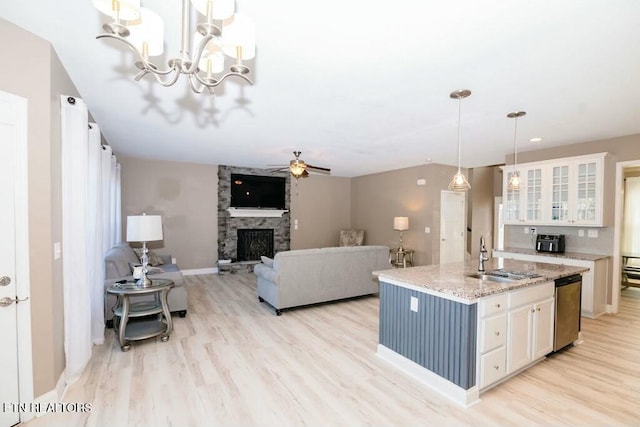 kitchen featuring light wood finished floors, white cabinetry, a sink, a stone fireplace, and dishwasher