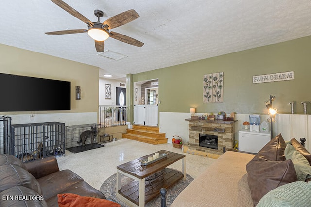 living room featuring ceiling fan, a fireplace, and a textured ceiling