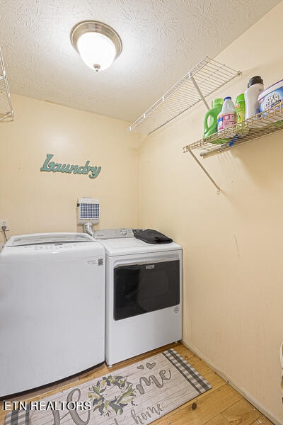 laundry area featuring a textured ceiling, independent washer and dryer, and light hardwood / wood-style floors