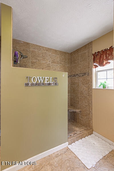 bathroom with tile patterned flooring, tiled shower, and a textured ceiling