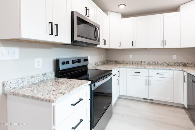 kitchen with light hardwood / wood-style floors, appliances with stainless steel finishes, light stone countertops, and white cabinets