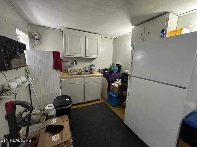 kitchen with a textured ceiling, white cabinetry, white fridge, and sink