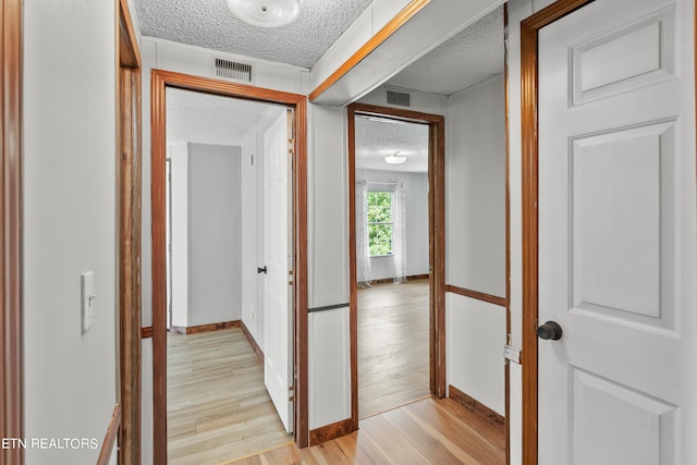 hall featuring light hardwood / wood-style floors and a textured ceiling