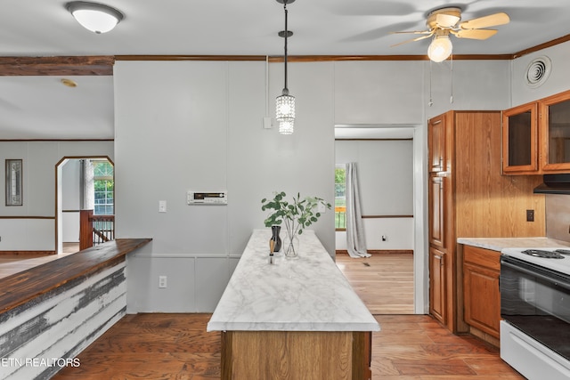 kitchen featuring electric range, hanging light fixtures, wood-type flooring, a kitchen island, and ornamental molding