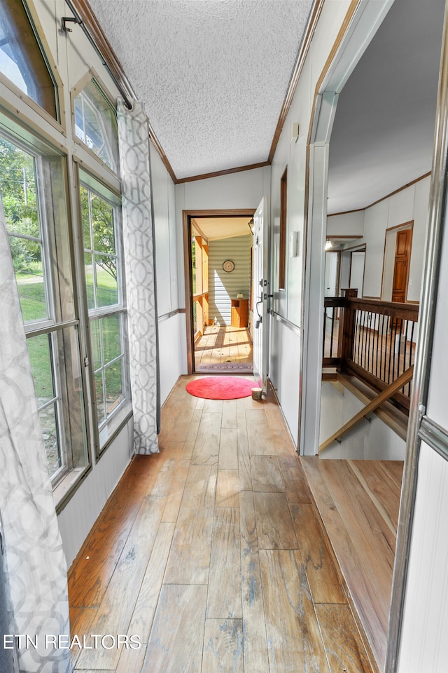 corridor featuring a textured ceiling, vaulted ceiling, light hardwood / wood-style flooring, and ornamental molding